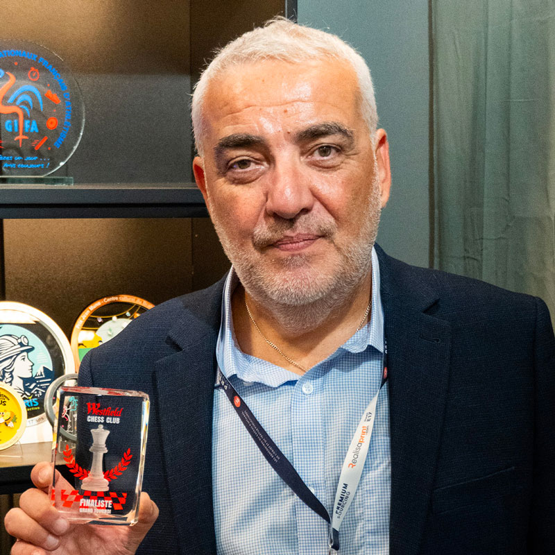 Serge Latour tenant un trophée en verre sur un stand professionnel.